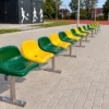 Ławka sportowa jednorzędowa ze stali nierdzewnej z zielonymi i żółtymi siedziskami przy boisku