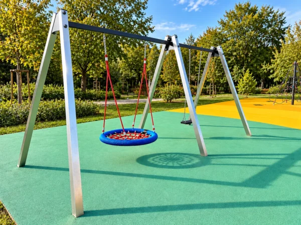 Stalowa huśtawka na plac zabaw z okrągłym bocianim gniazdem w kolorze niebiesko-czerwonym i siedziskiem płaskim
