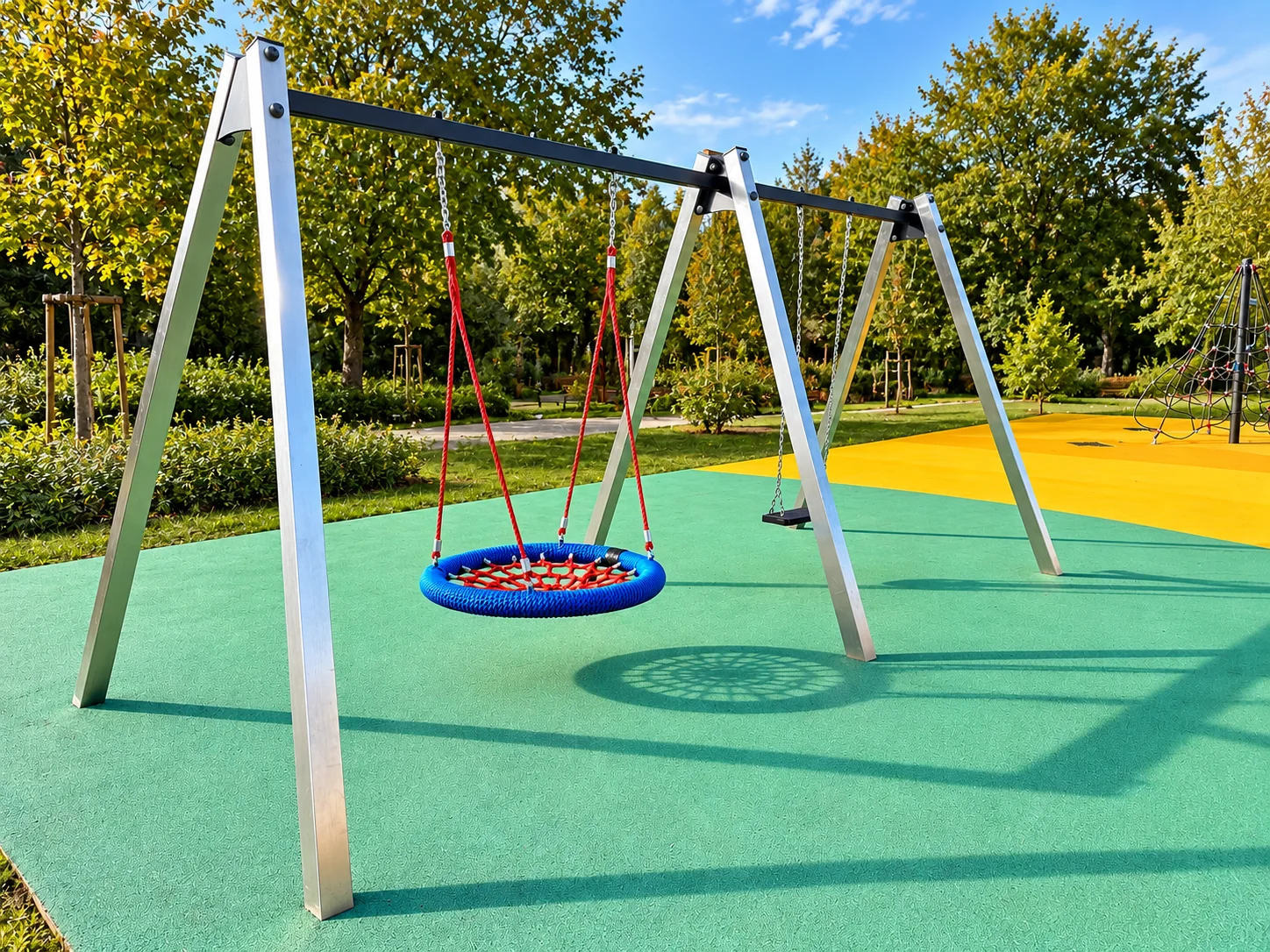 Stalowa huśtawka na plac zabaw z okrągłym bocianim gniazdem w kolorze niebiesko-czerwonym i siedziskiem płaskim